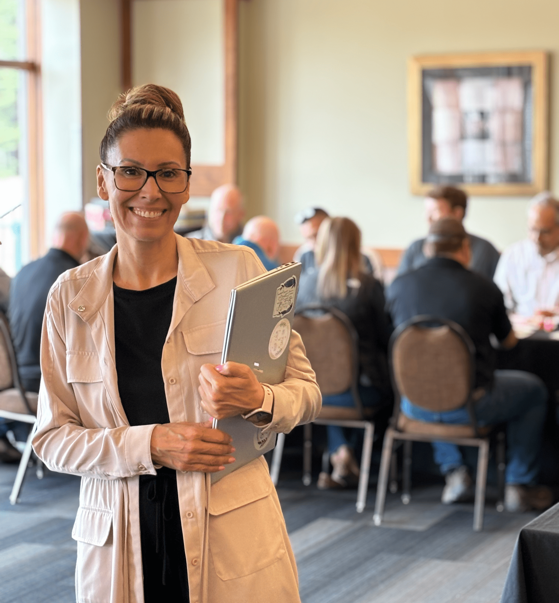 Darla stands holding her laptop in front of group seating together at a conference table.